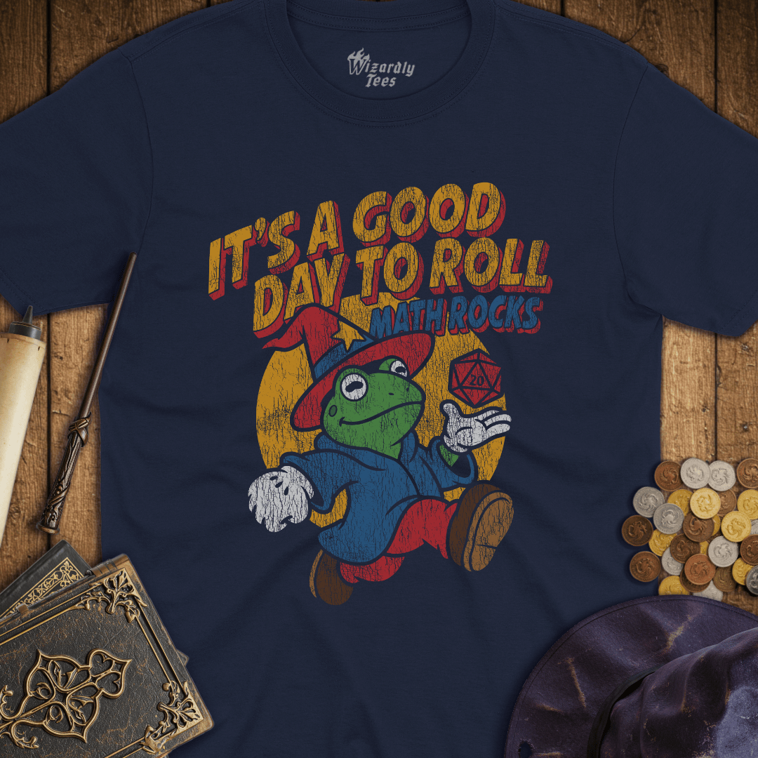 Navy blue t-shirt with a colorful graphic of a frog wizard holding a D20, text 'It's a good day to roll math rocks', on a wooden background.